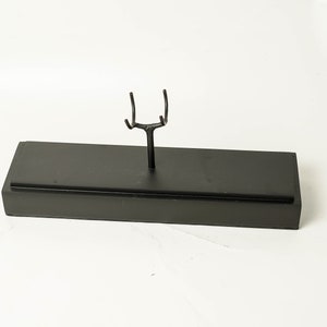 May include: A black metal display stand with a rectangular base and a Y-shaped top. The stand is designed to hold a single object.