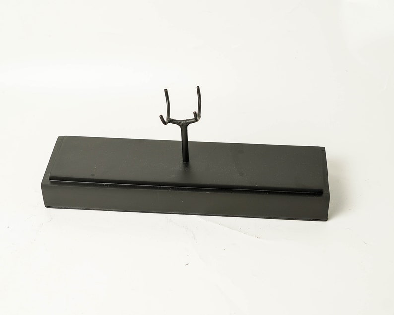 May include: A black metal display stand with a rectangular base and a Y-shaped top. The stand is designed to hold a single object.