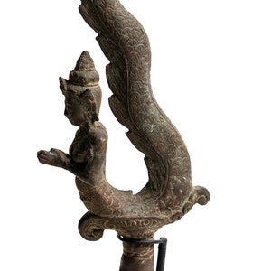 May include: A bronze sculpture of a mythical creature with a human-like torso and a tail that resembles a serpent. The creature is depicted in a kneeling position with its hands clasped together in prayer. The sculpture is intricately detailed and has a rich patina.