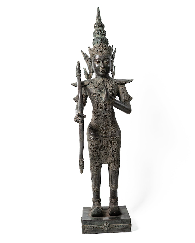Op de afbeelding: Een donker bronzen beeld van een staande figuur met een kroon en een boog en pijl. De figuur draagt ​​uitgebreide kleding en sieraden. Het beeld staat op een vierkante basis.
