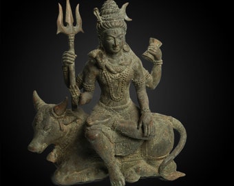 May include: A bronze statue of the Hindu god Shiva, seated on his mount, the bull Nandi. Shiva is depicted with a trident in his right hand and a cup in his left hand. The statue is intricately detailed and has a dark patina.