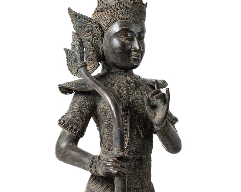 Op de afbeelding: Een gedetailleerd bronzen beeld van een godheid met een kroon en ingewikkelde houtsnijwerk. Het beeld houdt een staf vast en heeft een serene uitdrukking.