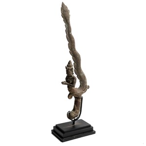 May include: A bronze sculpture of a mythical creature with wings and a human-like figure. The sculpture is mounted on a black wooden base.