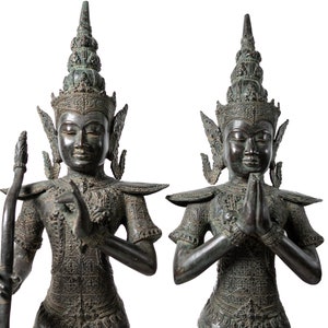 Op de afbeelding: Twee bronzen beelden van figuren in traditionele Thaise kleding, een houdt een staf vast en de andere heeft zijn handen in gebedshouding.