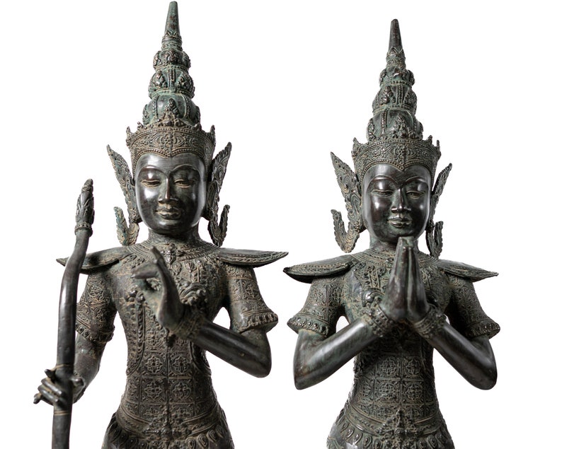 Op de afbeelding: Twee bronzen beelden van figuren in traditionele Thaise kleding, een houdt een staf vast en de andere heeft zijn handen in gebedshouding.