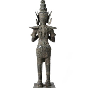 Op de afbeelding: Een bronzen beeld van een staande figuur met ingewikkelde details en een kroon. De figuur draagt ​​een traditionele kleding en heeft een serene uitdrukking.
