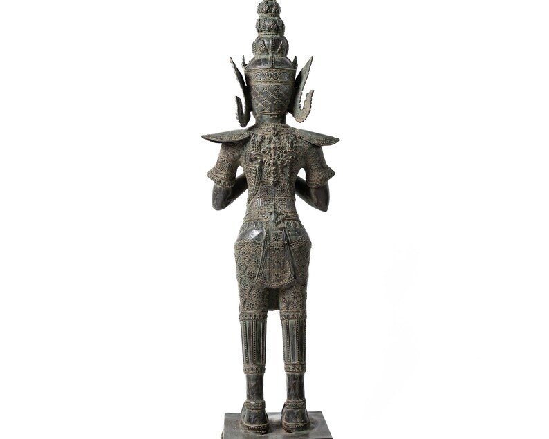 Op de afbeelding: Een bronzen beeld van een staande figuur met ingewikkelde details en een kroon. De figuur draagt ​​een traditionele kleding en heeft een serene uitdrukking.