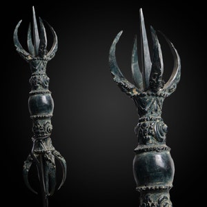 May include: A dark green metal ritual object with a pointed top and multiple curved prongs. The object has intricate details and a round, bulbous middle section.