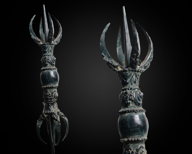 May include: A dark green metal ritual object with a pointed top and multiple curved prongs. The object has intricate details and a round, bulbous middle section.