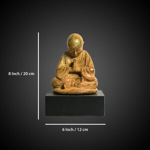 May include: A small, gold-colored ceramic statue of a seated Buddha figure with hands in prayer position. The statue is 8 inches tall and 6 inches wide.