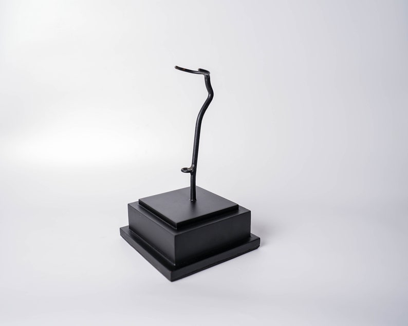 May include: A black metal display stand with a curved arm, perfect for showcasing small items like figurines or jewelry.