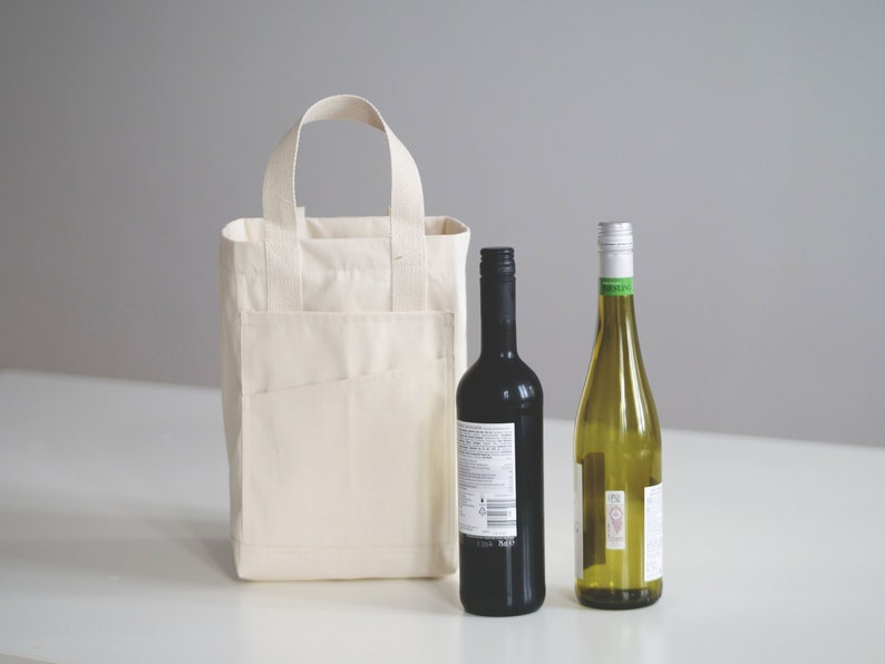 May include: A white canvas tote bag with a pocket on the front, holding a bottle of red wine and a bottle of white wine.