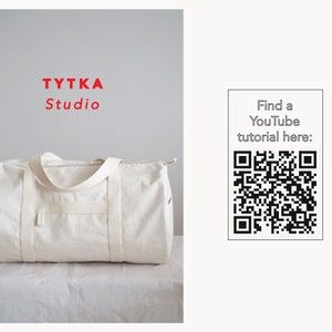 May include: A white canvas duffel bag with a zipper closure and two handles. The bag is sitting on a white surface. The text "TYTKA Studio" is in red letters above the bag. A QR code is on the right side of the image with the text "Find a YouTube tutorial here:".