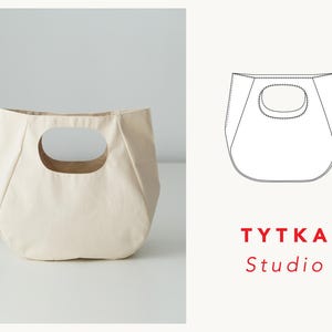 May include: A cream-colored canvas tote bag with a unique cut-out handle. The bag is made by TYTTKA Studio.
