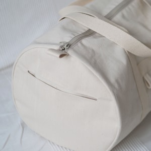 May include: A white canvas duffel bag with a zipper closure and two straps. The bag has a small pocket on the side.