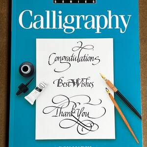 May include: A teal book titled "Calligraphy" from the "First Steps Series" with a white page featuring calligraphy phrases "Congratulations", "Best Wishes", and "Thank You". Includes ink, a pen, and a tube of white paint.