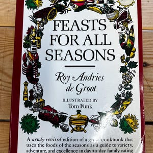 May include: A red hardcover cookbook titled "Feast for All Seasons" by Roy Andries de Groot, illustrated by Tom Funk. The cover features a colorful illustration of various foods and seasonal items.