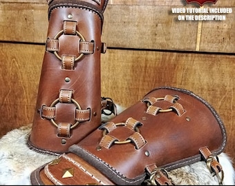 May include: A pair of brown leather bracers featuring brass-colored metal rings, studs, and pyramid-shaped accents. The bracers are constructed with stitched leather straps and include text indicating a digital download and video tutorial.