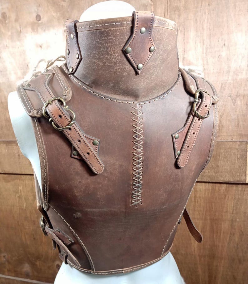 Puede incluir: Armadura de pecho de cuero marr&oacute;n con cuello alto y correas para los hombros. La armadura presenta costuras decorativas, remaches met&aacute;licos y hebillas ajustables. El cuero tiene un acabado envejecido, d&aacute;ndole un aspecto vintage.