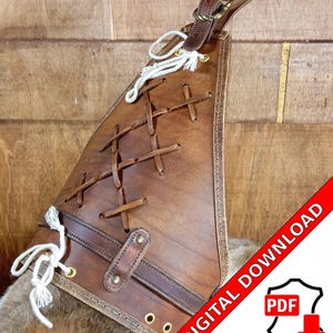 Könnte beinhalten: Ein brauner Lederarmschutz mit einem Kreuzmuster und einem Riemen. Der Armschutz hat eine weiße Schnur mit einem Quasten. Das Bild enthält den Text "DIGITALER DOWNLOAD PDF" in Rot.