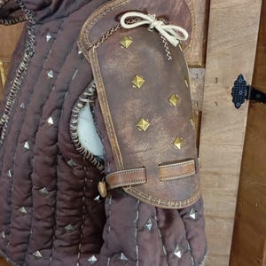 May include: A brown leather padded armour with metal studs and a leather shoulder guard with metal studs and a strap.