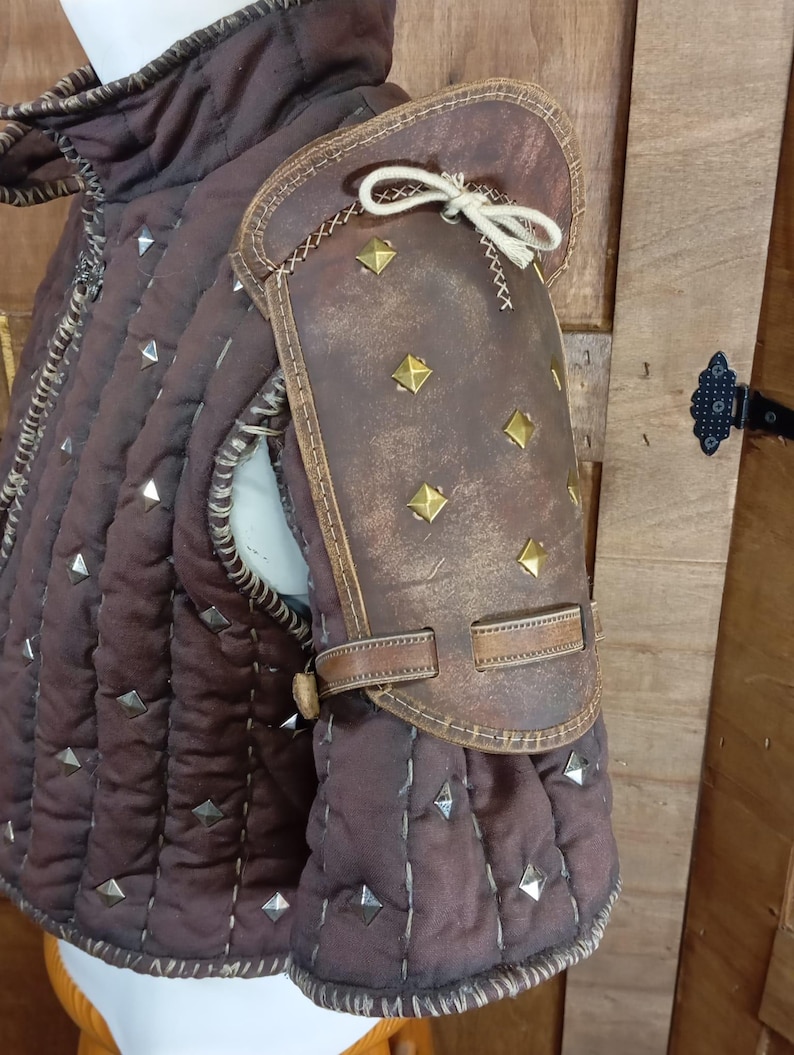 May include: A brown leather padded armour with metal studs and a leather shoulder guard with metal studs and a strap.