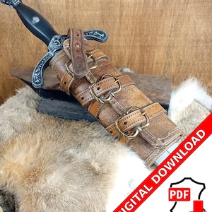 Może przedstawiać: Brązowa pochwa skórzana z metalowymi klamrami i paskami do miecza. Pochwa leży na drewnianej powierzchni, pod którą znajduje się futrzany dywan. Na zdjęciu widoczny jest tekst "POBIERANIE CYFROWE" i "PDF".