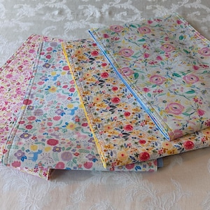 May include: Four table runners with floral patterns. The runners are made of fabric and have a light blue, pink, yellow, and white color scheme.