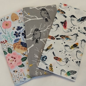 May include: Three fabric squares with different bird and floral patterns. The first square is light blue with a floral pattern and a bluebird. The second square is gray with a branch and birds. The third square is white with a black and white bird pattern.