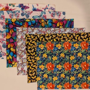 May include: Six colorful placemats with butterfly and floral patterns. The placemats are made of fabric and have a variety of colors, including pink, blue, green, yellow, and red.