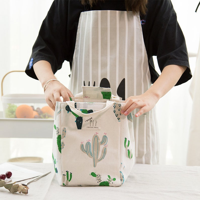 May include: A white canvas lunch bag with a green cactus print. The bag has two handles and a zipper closure.