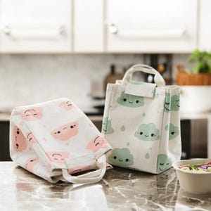 May include: Two white canvas lunch bags with cute cartoon cloud designs. One bag has pink clouds and the other has green clouds.