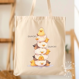 May include: A beige canvas tote bag with a graphic of a stack of rubber duckies. The ducks are yellow and white and are stacked on top of each other. The text "Quack!" appears twice on the bag.