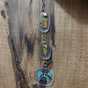 May include: A silver keychain with three clear charms featuring cartoon images of Pokemon characters. The charms are a yellow caterpillar, a yellow cocoon, and a blue and yellow bee.