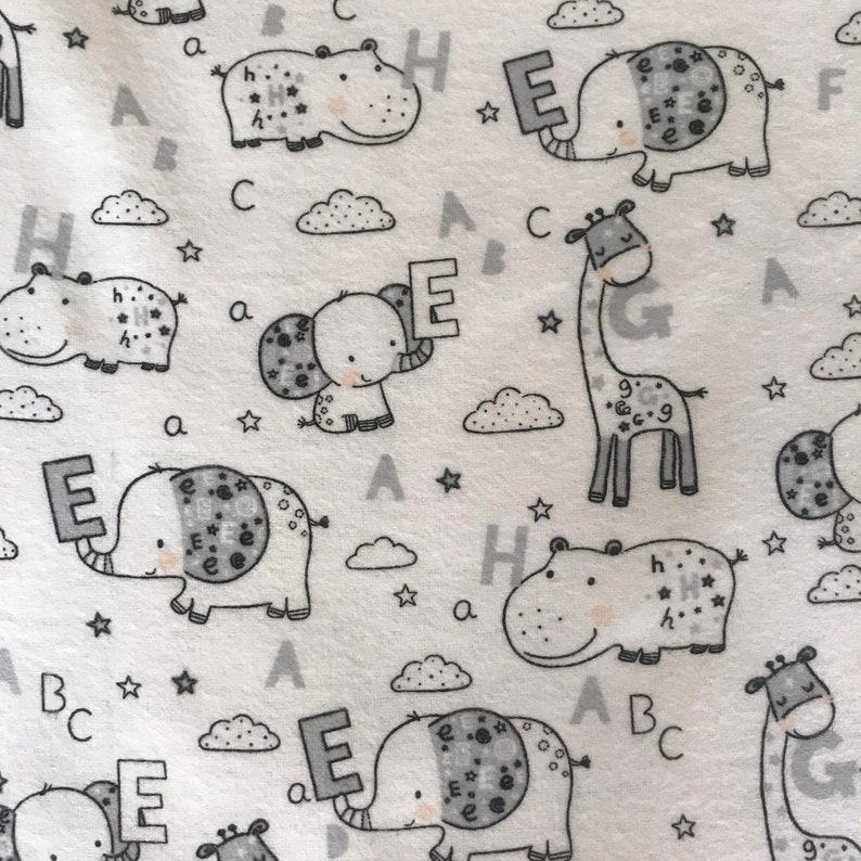 Puede incluir: Tela blanca con un patr&oacute;n repetido de ilustraciones de animales en blanco y negro. Los animales incluyen elefantes, hipop&oacute;tamos, jirafas y nubes. Las letras A, B, C, E, G y H est&aacute;n dispersas por todo el patr&oacute;n.