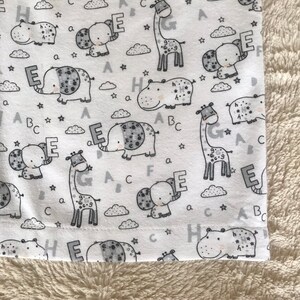 Puede incluir: Tela blanca con un patr&oacute;n repetido de ilustraciones de animales en blanco y negro. Los animales incluyen elefantes, hipop&oacute;tamos y jirafas. Cada animal sostiene una letra del alfabeto. Las letras son E, A, B, C, G y H.