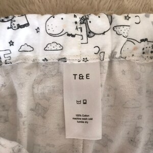 Puede incluir: Pantal&oacute;n blanco de algod&oacute;n con estampado en blanco y negro de animales y estrellas. El pantal&oacute;n tiene una etiqueta de cuidado blanca que dice "T&E", "100% algod&oacute;n", "lavar a m&aacute;quina con agua fr&iacute;a" y "secar en secadora a baja temperatura".