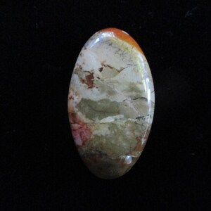 May include: A smooth, oval-shaped cabochon with a swirling pattern of brown, white, and green colors.