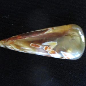 May include: A polished, teardrop-shaped gemstone with a mix of colors. The stone features translucent areas with brown, orange, and white patterns. The gem has a smooth, glossy surface and a pointed end.