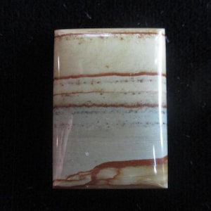 May include: A rectangular, light brown and white stone with a layered pattern. The stone has a smooth, polished surface.