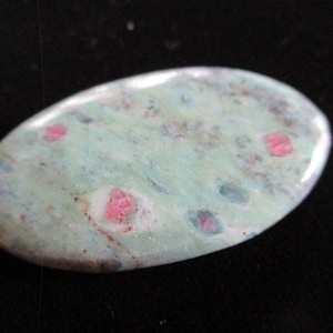 May include: A light green oval-shaped stone with pink and blue inclusions. The stone is polished and smooth.