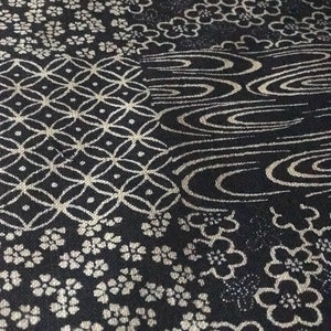 May include: Black fabric with a white geometric pattern. The pattern includes a repeating design of flowers, waves, and a grid.