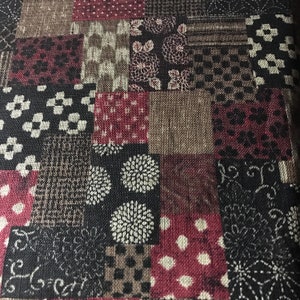 May include: A patchwork fabric with a variety of patterns and colors. The design includes squares of black, burgundy, brown, and tan, with floral, geometric, and dotted motifs. The fabric has a textured appearance.