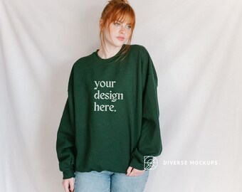 May include: A dark green sweatshirt with the text "your design here" printed on the front. The sweatshirt is being worn by a person with red hair.