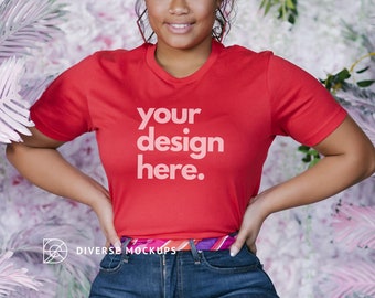 May include: A red t-shirt with the text "your design here." printed on the front. The shirt is being worn by a person with dark hair and a light skin tone. The person is standing in front of a pink floral background.