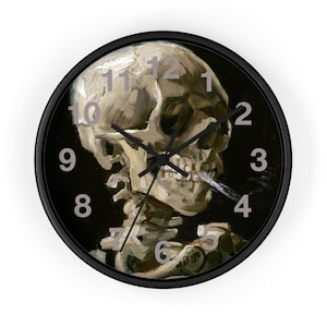 May include: A black wall clock with a skull design. The skull is painted in beige and grey, set against a black background. The clock has black hands and silver numerals.