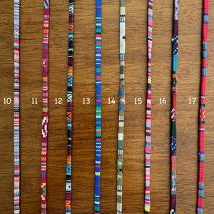 May include: Ten different colorful woven cords with various patterns. The cords are all approximately the same length and are displayed against a wooden background.