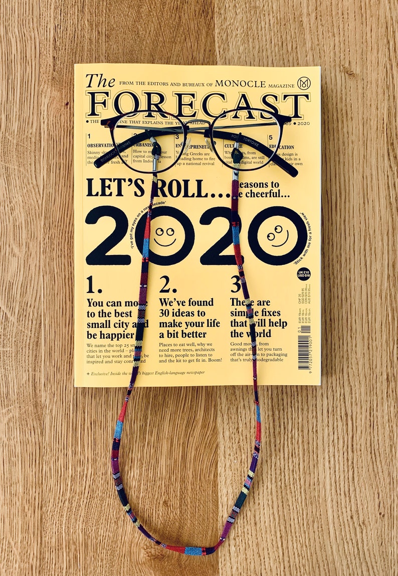 May include: A yellow magazine with the title "The Forecast" and the year "2020" printed in black. The magazine is held by a pair of black glasses with a colorful beaded strap.