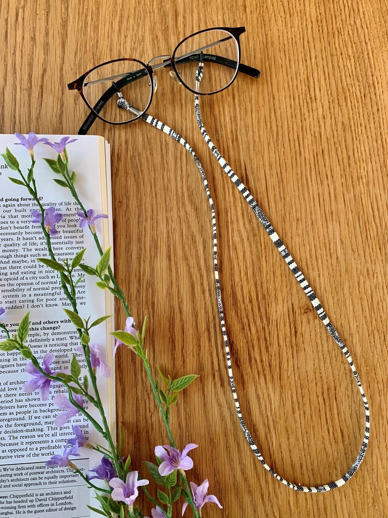 May include: Black and white striped glasses chain with a pair of eyeglasses on a wooden surface. The glasses chain is made of beads and has a simple design.