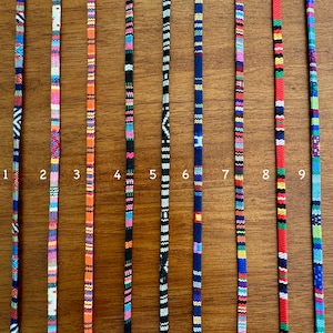 May include: Nine colorful woven cords, numbered 1 through 9, are displayed against a woodgrain background. Each cord features a unique pattern of stripes and colors.
